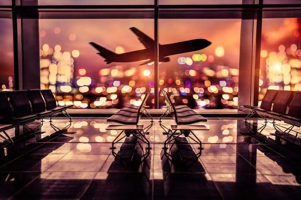 Empty airport lounge shot at night in front of the city skyline with airplane taking off against the bright lit of the city.