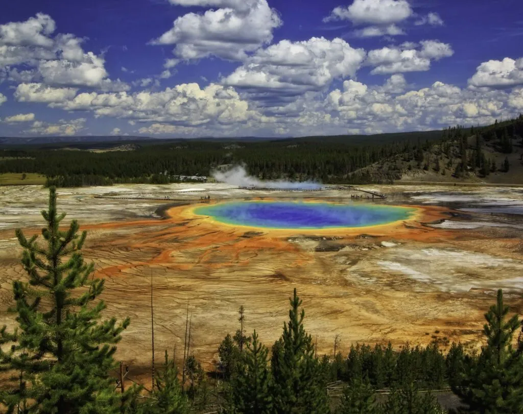 A wide-angle view of Grand Prismatic Spring with puffy clouds overhead in Yellowstone National Park, Wyoming.