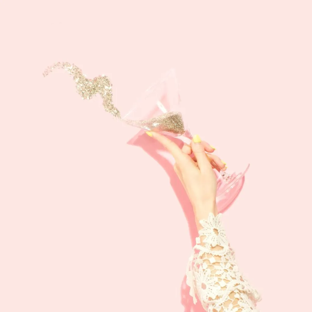 Woman holding martini glass filled with glitter. Photo by Amy Shamblen on Unsplash