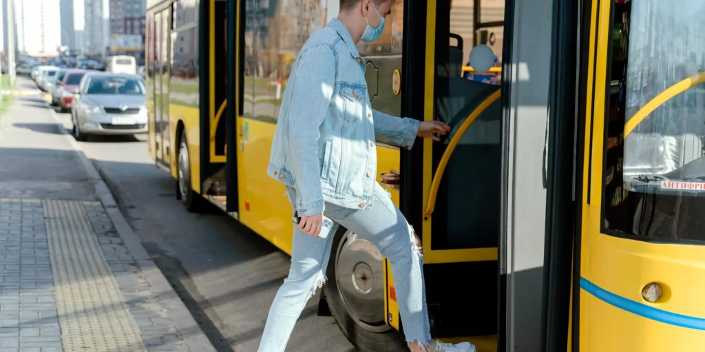 Young man in a denim jacket and face mask stepping onto an airport shuttle bus